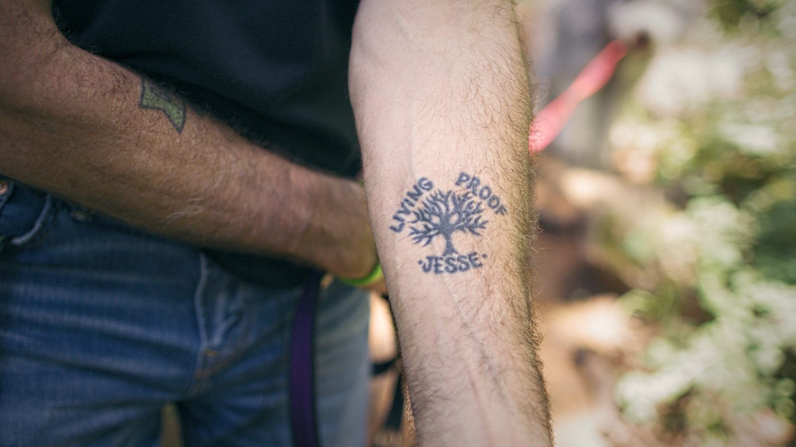 A 'Living Proof — Jesse' tattoo on a forearm